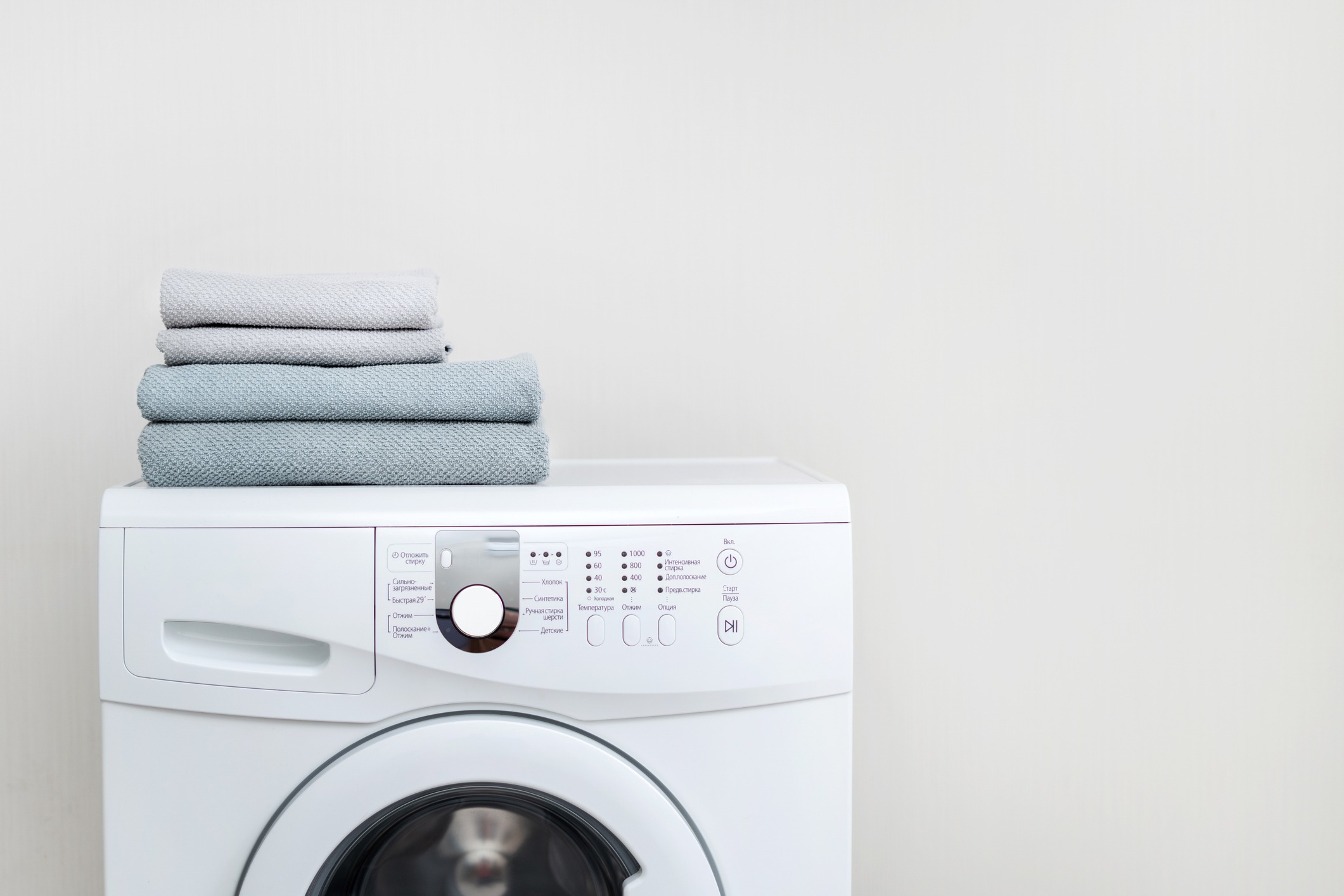 Laundry concept. Cropped photo of white and modern washing machine with fresh towel on top standing isolated inside bright apartment light interior